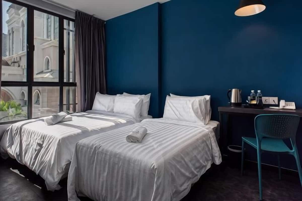 A hotel room with a large bed, a desk, a chair, and a view of buildings through a window.