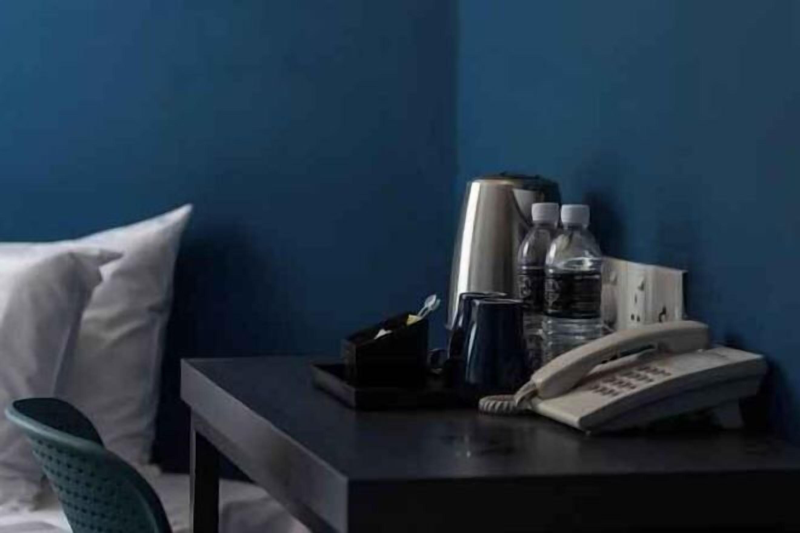 Une chambre d’hôtel avec un lit, une table de chevet avec un téléphone, des bouteilles d’eau et une tasse.