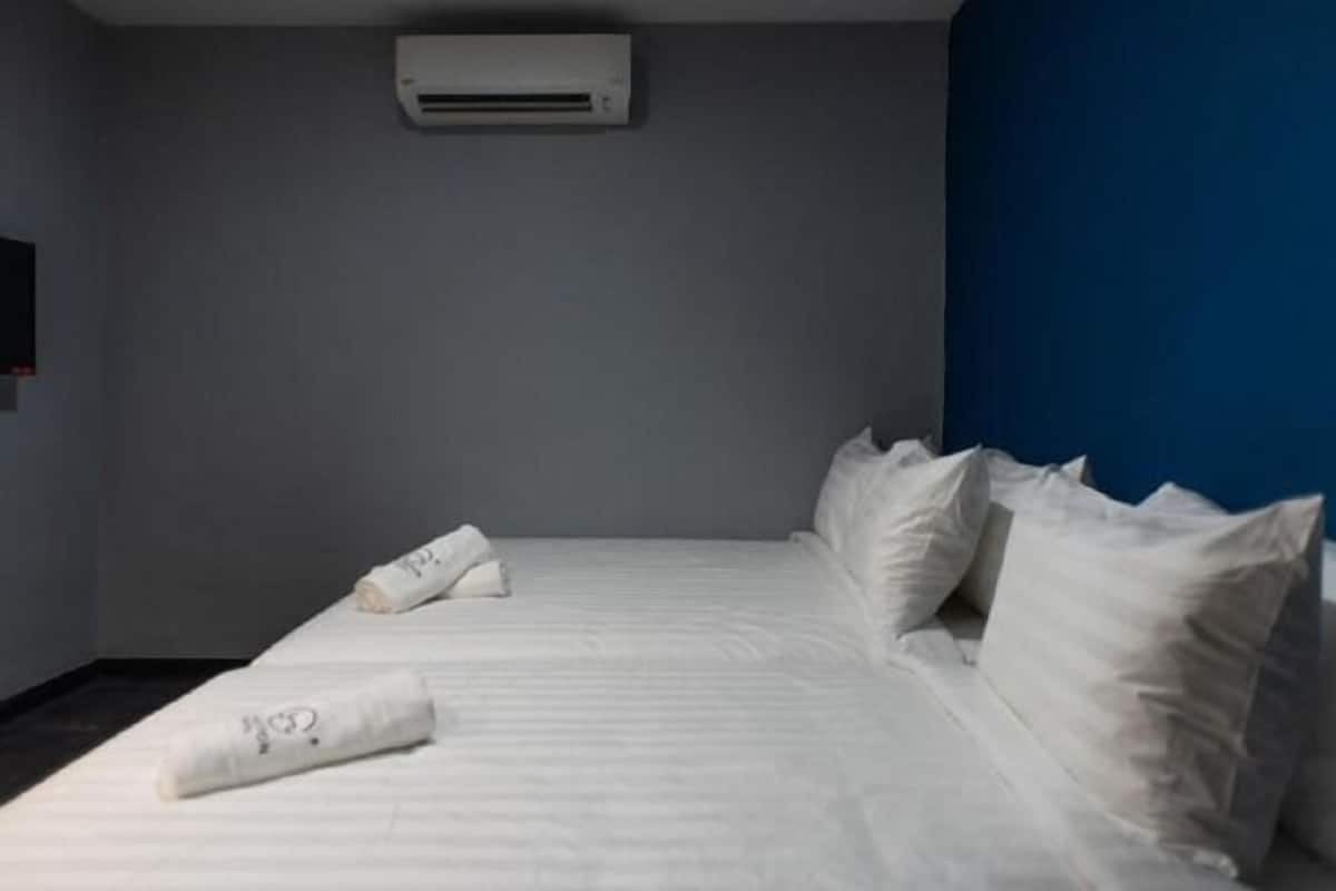 A hotel room with a bed, pillows, a wall-mounted air conditioner, and a blue accent wall.