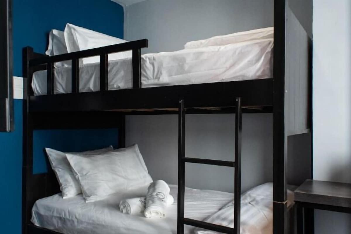 Un letto a castello con biancheria e cuscini bianchi, una scala e un tavolino.