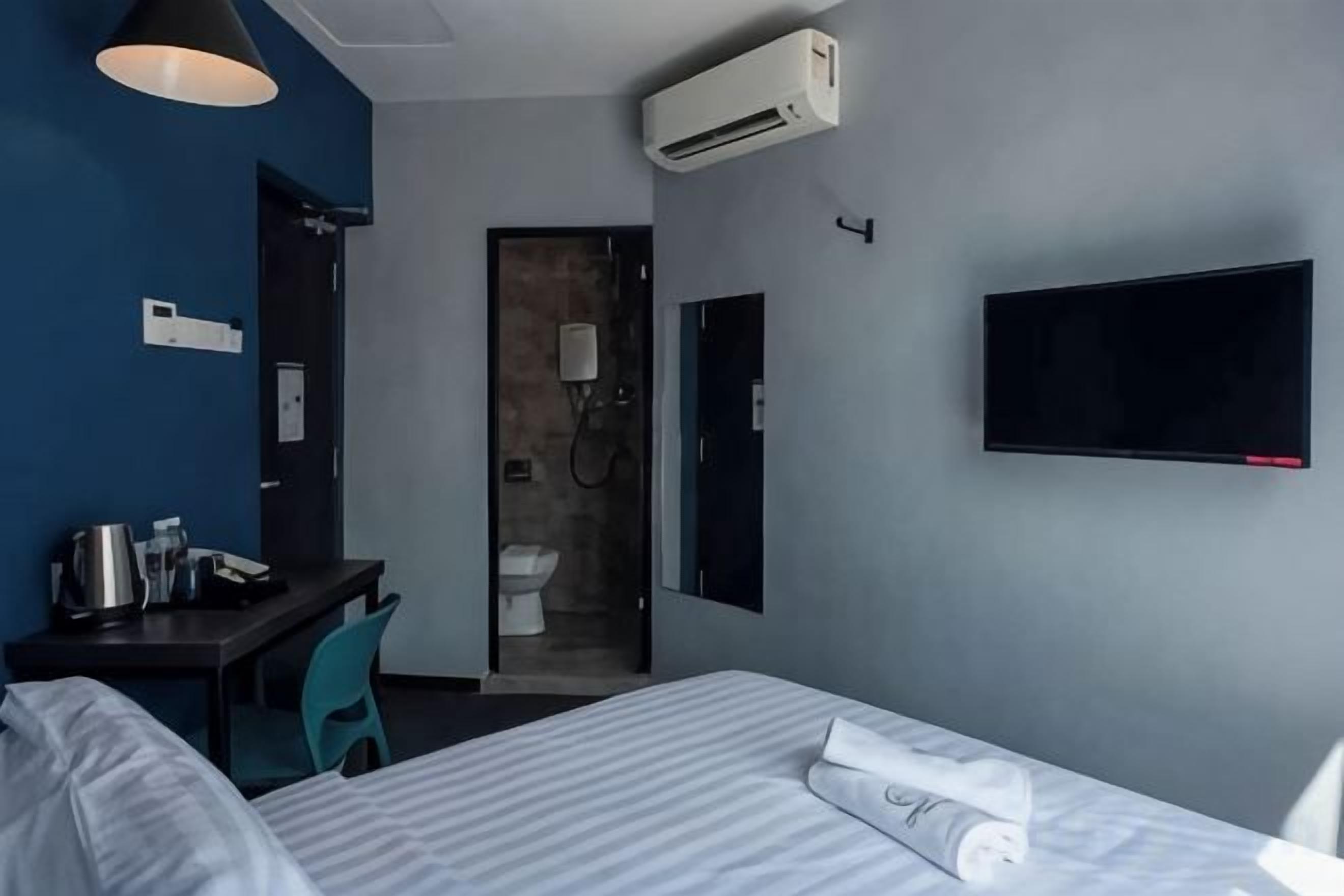 Ein Hotelzimmer mit einem Bett, einem Schreibtisch mit Stuhl, einem an der Wand befestigten Fernseher und einer Klimaanlage.