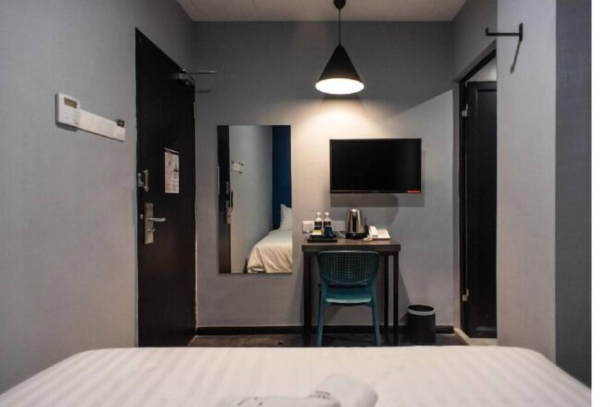 A hotel room with a bed, a desk with a chair, a television, and a mirror.