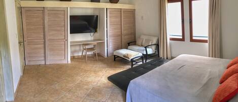 A bedroom with a bed, a desk, a chair, a television, and a window.