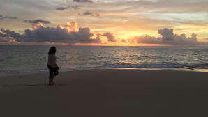 A beach scene with a person standing on the sand, facing the ocean during sunset. - 2-bed Designer Apartment Sleeps 4, Resort Pool (Lowlands)