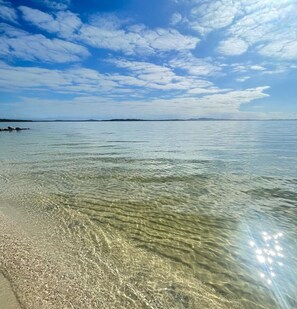 Una playa despejada con aguas poco profundas, una orilla arenosa y una línea costera distante con rocas.