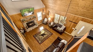 Un salon chaleureux avec une cheminée, des canapés en cuir, un téléviseur et un plafond en bois.