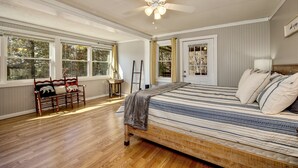 Une chambre à coucher avec un grand lit, un banc en bois, un ventilateur de plafond et une fenêtre donnant sur des arbres.