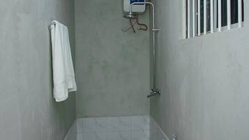 A small, narrow bathroom with a toilet, a shower, and a window with bars.