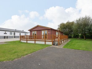 Ein Bungalow mit Holzterrasse und kleiner Veranda, umgeben von Rasenflächen und einem gepflasterten Weg.