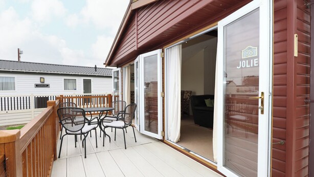 Un patio couvert avec une table et des chaises, une porte-fenêtre coulissante avec une plaque nominative et une terrasse en bois.