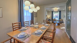 Un coin repas avec une longue table en bois, dressée pour quatre personnes, entourée de chaises en bois. Des luminaires sphériques sont suspendus au-dessus de la table.