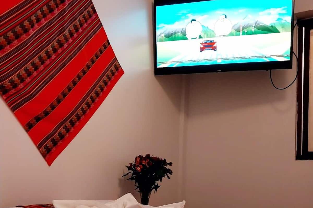 A hotel room with a bed, a television mounted on the wall, and a decorative red and black patterned fabric on the wall.