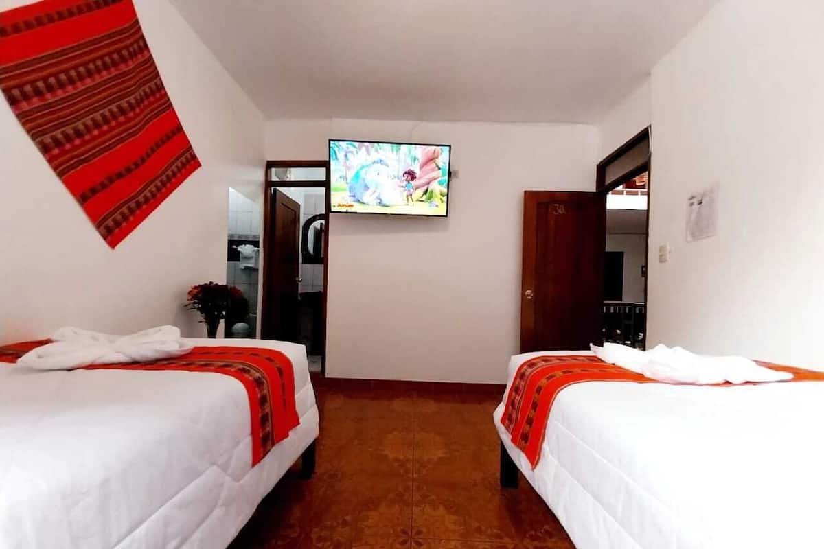 A hotel room with two beds, a TV on the wall, and a red patterned wall hanging.