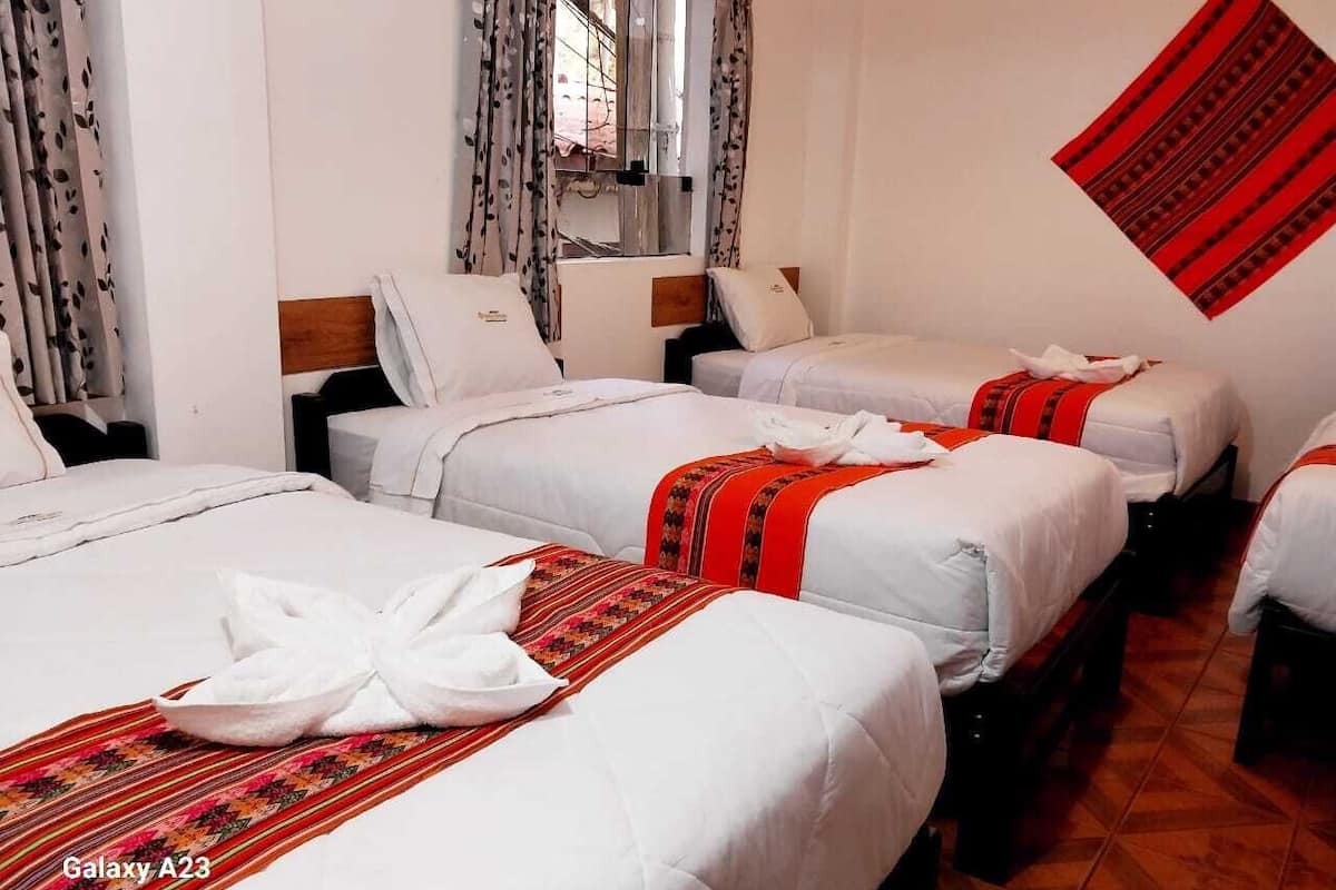 A hotel room with three beds, each with white bedding and red accents.