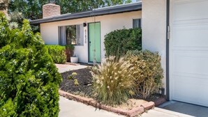 A modern house with a green door, a garage, and a landscaped garden with various plants. - Moonrise Ranch|Yoga Sun Room|Cowboy Pool (Joshua Tree)
