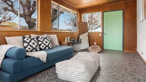 A room with a blue sofa, a white ottoman, and a green door. - Moonrise Ranch|Yoga Sun Room|Cowboy Pool (Joshua Tree)