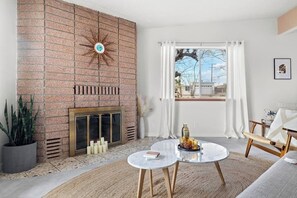 A living room with a brick fireplace, a round coffee table, a sofa, and a window with curtains.