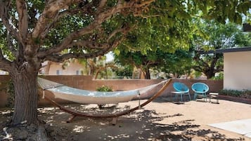 A hammock under a tree, a blue chair, and a patio area with a building in the background.