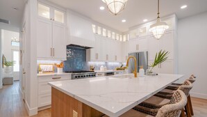 Une cuisine moderne avec des meubles blancs, un grand îlot central et un coin repas doté de chaises en osier.