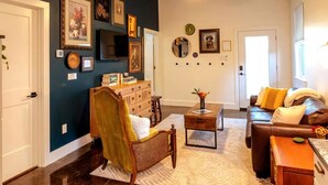 A living room with a dark blue accent wall, a wooden chair, a brown leather sofa, a coffee table, and a ceiling fan. - El Gato Bandito (Denton)
