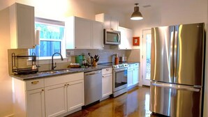 A modern kitchen with white cabinets, stainless steel appliances, and a granite countertop. - El Gato Bandito (Denton)