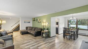 A spacious living area with a sectional sofa, a dining table with chairs, and a staircase leading to another level.