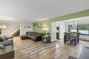 A spacious living area with a sectional sofa, a dining table with chairs, and a staircase leading to another level.