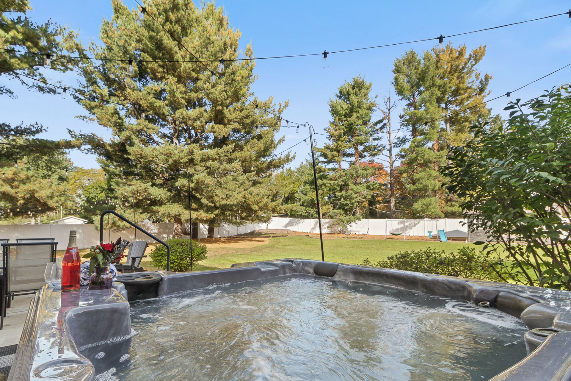 A hot tub with a clear view of the surrounding yard, including trees and a fenced area.
