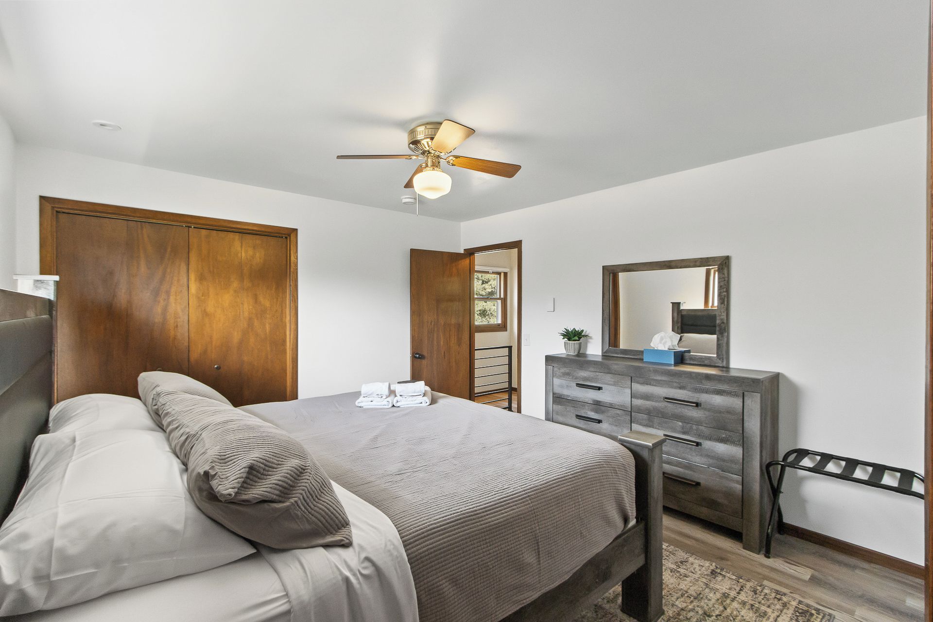 A bedroom with a bed, a dresser, a mirror, and a ceiling fan.
