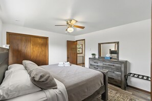 A bedroom with a bed, a dresser, a mirror, and a ceiling fan.