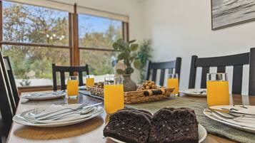 Ein Frühstückstisch mit Stühlen, Tellern, Besteck, Gläsern Orangensaft und einem Schokoladenkuchen.
