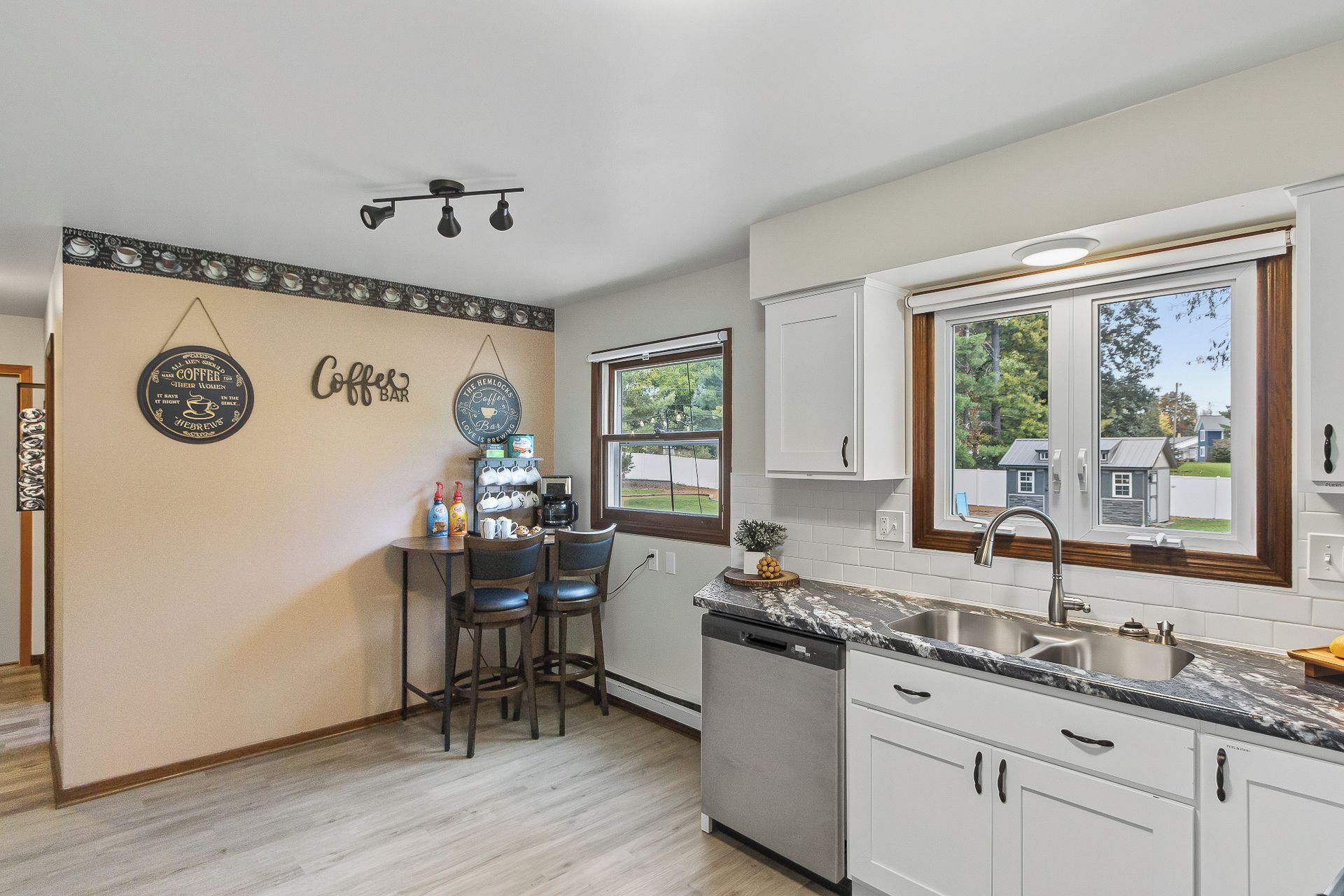 A kitchen with a coffee bar, bar stools, a dishwasher, and a window with a view of houses.