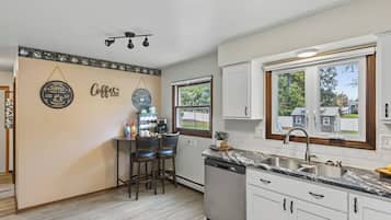 A kitchen with a coffee bar, bar stools, a dishwasher, and a window with a view of houses.