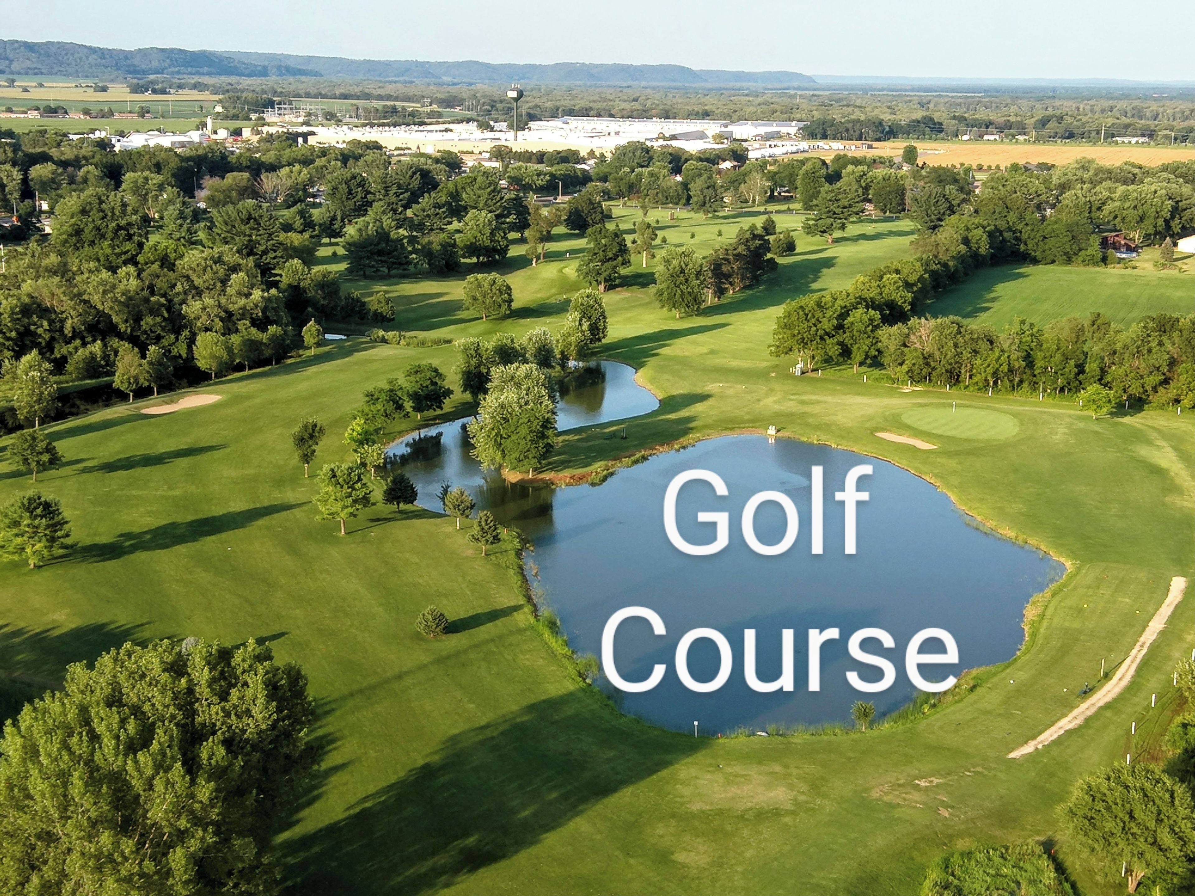 A golf course with a pond, trees, and a distant view of buildings.