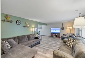 A living room with a sectional sofa, a flat-screen TV, a lamp, and a guitar on the wall.