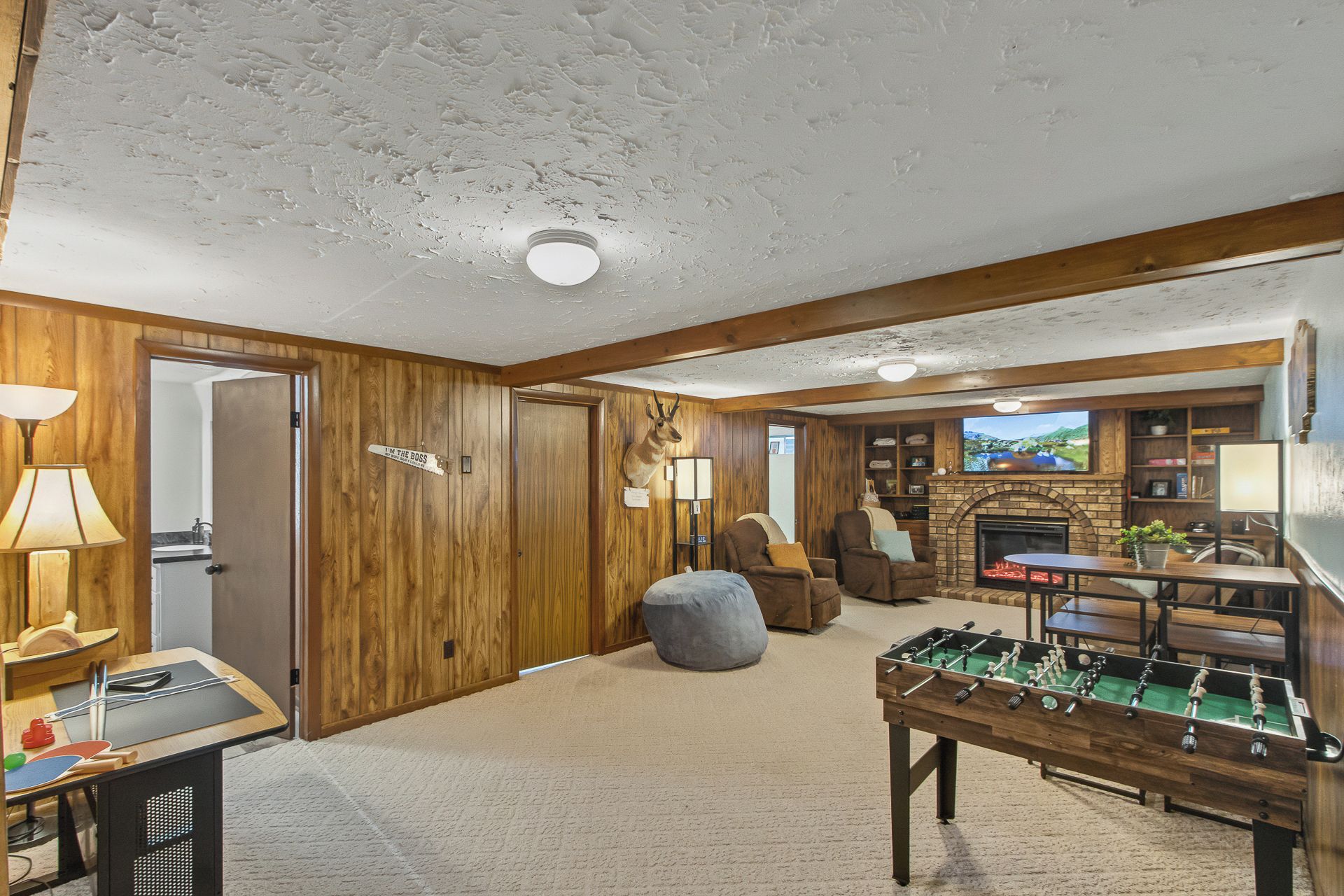 A cozy living room with a fireplace, a foosball table, and a television mounted above it.