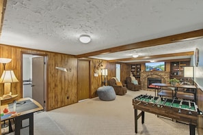 A cozy living room with a fireplace, a foosball table, and a television mounted above it.