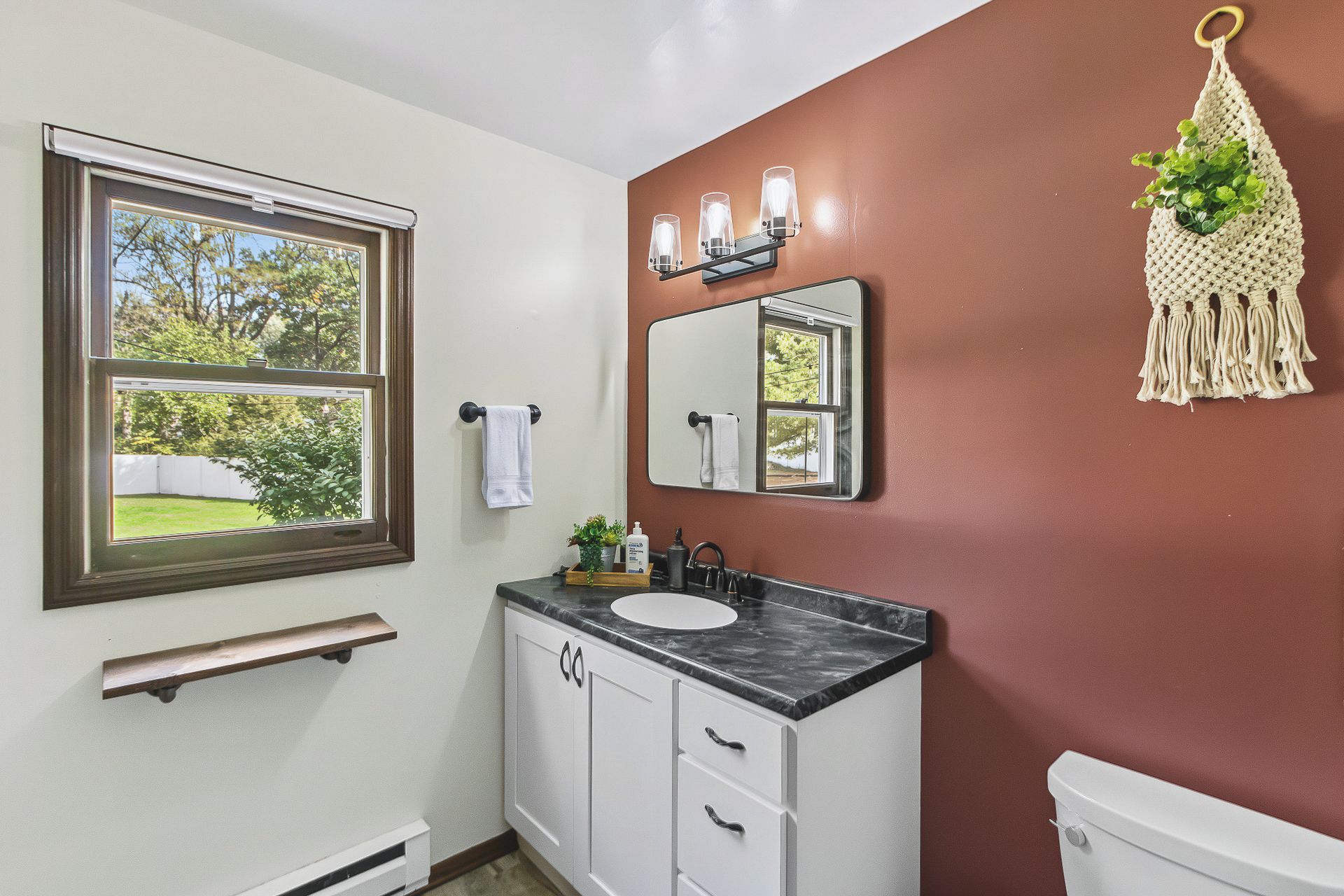 A bathroom with a window, a sink, a mirror, and a toilet.