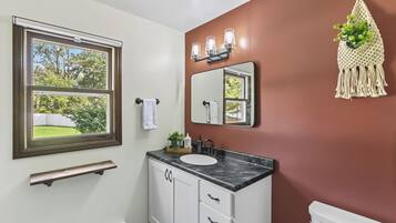 A bathroom with a window, a sink, a mirror, and a toilet.