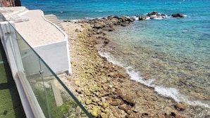 A clear view of a rocky shoreline with a glass railing overlooking the ocean. - Seaview Resort Boca Sami (Sint Michiel)