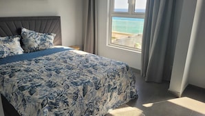 A bedroom with a bed, a nightstand, a window with a view of the sea, and a map on the wall. - Seaview Resort Boca Sami (Sint Michiel)