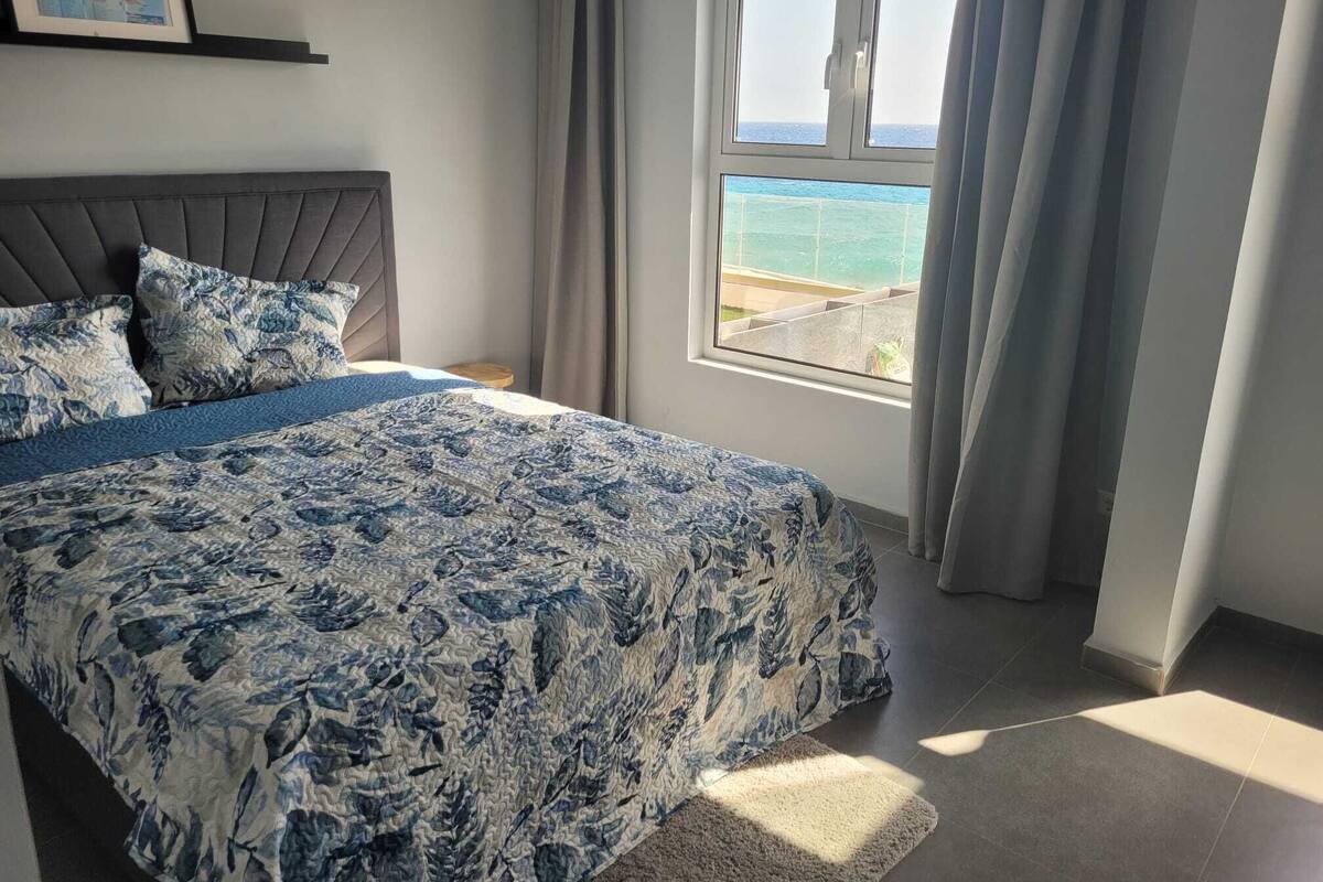 Quarto com cama, mesa de cabeceira, janela com vista para o mar e mapa na parede.