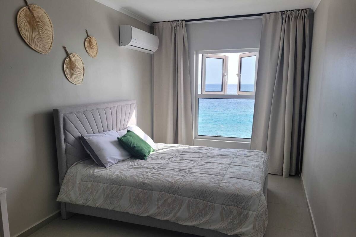 Quarto com cama, janela com cortinas e aparelho de ar condicionado.