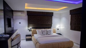 A modern bedroom with a large bed, a desk, and a TV. - Casa De Los Reyes Luxury Apartments (Abuja)