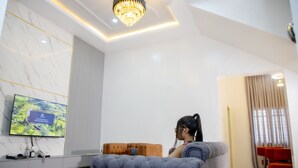 A modern living room with a large flat-screen TV, a tufted sofa, and a chandelier. - Casa De Los Reyes Luxury Apartments (Abuja)