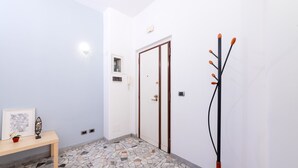 Un couloir avec un sol carrelé, un banc en bois, un porte-manteau et une porte dotée d’une poignée.
