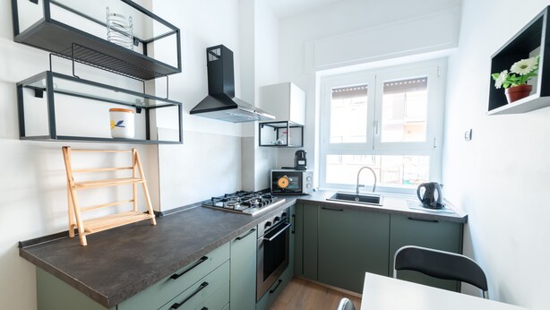 Une cuisine moderne équipée d’une cuisinière à gaz, d’un four et d’un micro-ondes encastré. Une fenêtre laisse entrer la lumière naturelle et offre une vue sur l’extérieur.