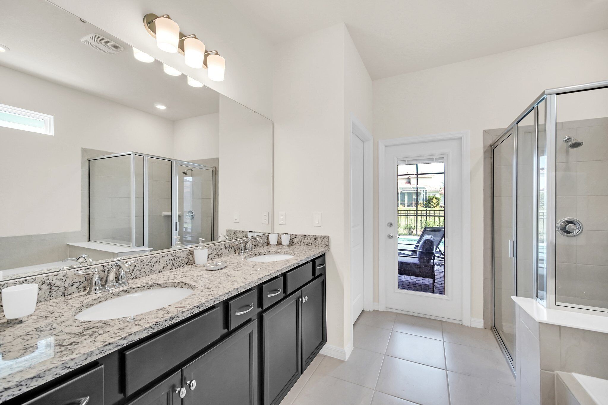 A modern bathroom with a double sink vanity, a large mirror, and a glass shower enclosure.