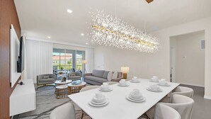 Una habitación de hotel moderna con comedor, un conjunto de sofás y una araña.