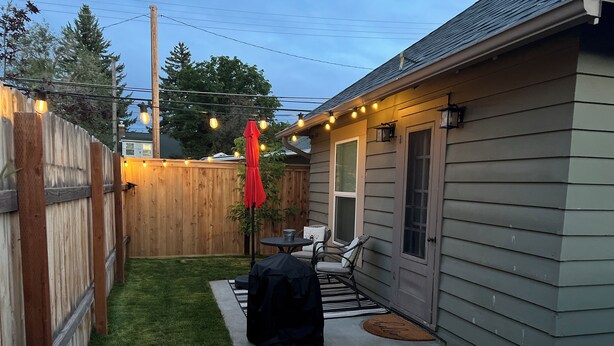 A backyard with a barbecue grill, a small table with chairs, and a wooden fence. - Cozy cottage in downtown Hamilton in the heart of the Bitterroot Valley.  (Hamilton)